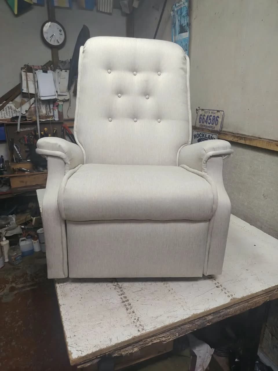 Sillón reclinable tapizado en tela crema con respaldo capitoné y ribete cosido