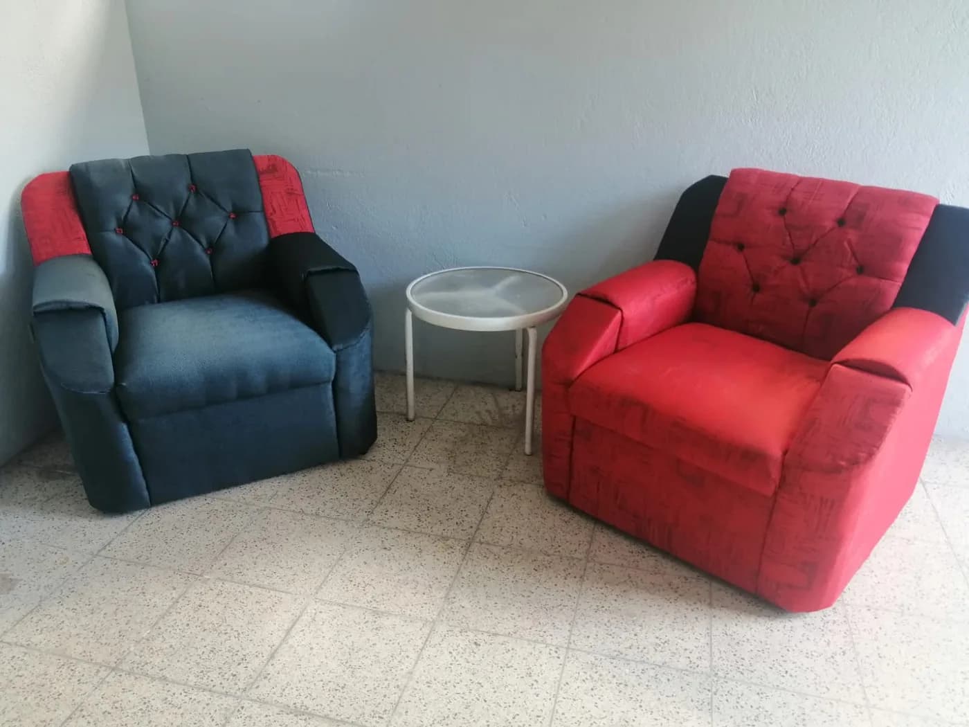 Dos sillones reclinables tapizados a dos tonos, uno rojo y uno azul, con paneles negros y respaldo capitoné