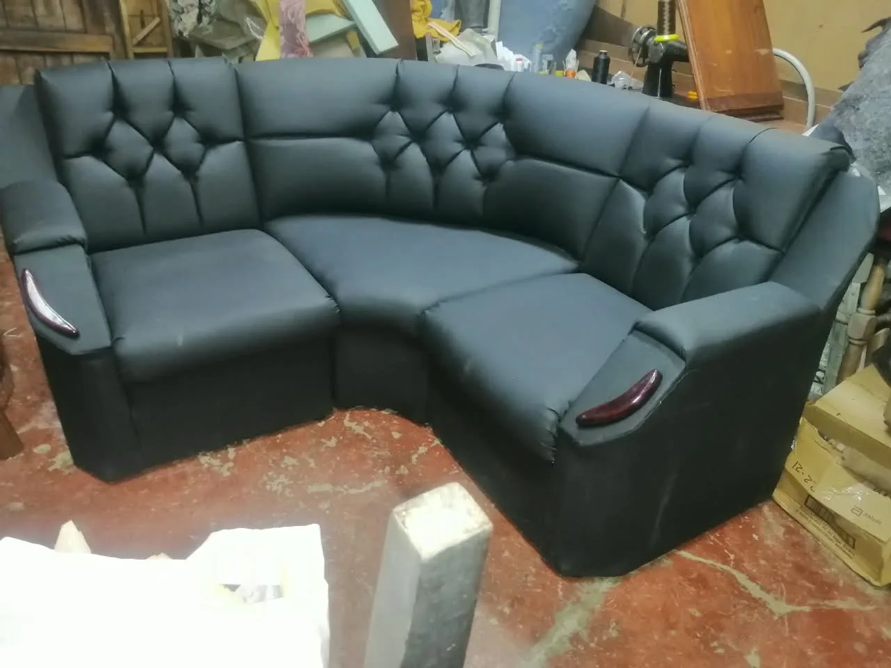 Seccional curvo tapizado en cuero sintético negro con respaldos capitoné y detalles de madera caoba