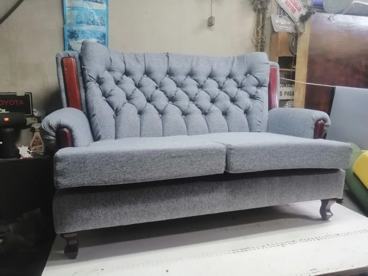 Sofá de dos puestos tapizado en tela jaspeada gris con respaldo capitoné y apliques de madera barnizada
